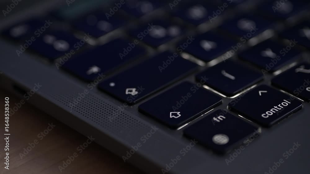 A close-up video of a person's finger pressing the right arrow key on a sleek laptop keyboard. The video highlights the dark keycaps, modern design, and the perforated speaker grille on the device. A close-up video of a person's finger pressing the right arrow key on a sleek laptop keyboard. The video highlights the dark keycaps, modern design, and the perforated speaker grille on the device.