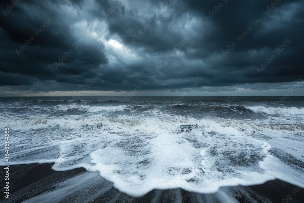 Obraz premium Dramatic seascape featuring dark ominous storm clouds and crashing waves on a black sand beach