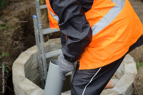 Worker in protective gear installing and inspecting septic system pipes inside a manhole at a private house, ensuring proper drainage, maintenance, and local wastewater management