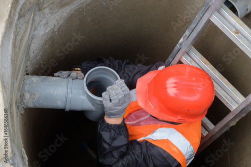 Worker in protective gear installing and inspecting septic system pipes inside a manhole at a private house, ensuring proper drainage, maintenance, and local wastewater management