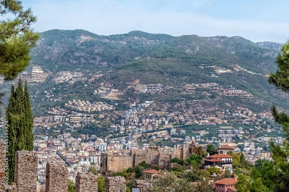 Obraz premium Scenic view of Alanya, Turkey, framed by historic Alanya Castle walls. City architecture and mountains under clear sky highlight the charm of this popular Mediterranean destination