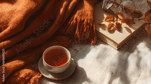 Warm autumnal still life with teacup, blanket, and book.