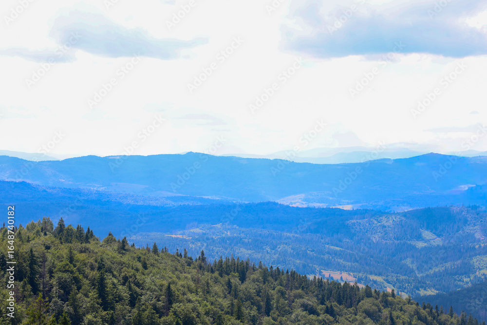 Fototapeta premium Endless mountain ranges covered with dense forests create a layered panoramic view that gradually fades into a blue haze. The foreground shows green hills, emphasizing the grandeur and beauty of the n