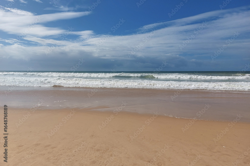 Obraz premium Deserted sandy beach with waves and cloudy sky. Tranquil seascape photography.