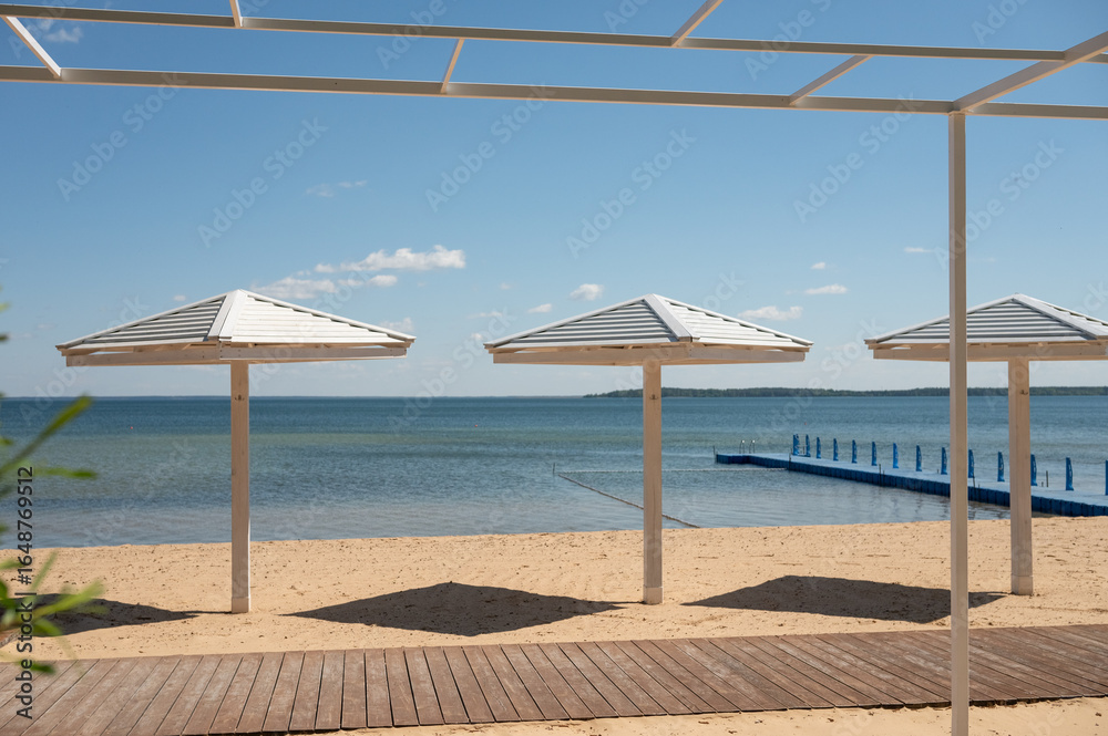 Fototapeta premium Modern beachfront gazebo with umbrellas and pier on sandy shoreline