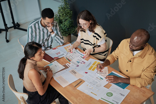 High angle view of business people sitting at table examining documents with charts and planning new strategy in team at meeting