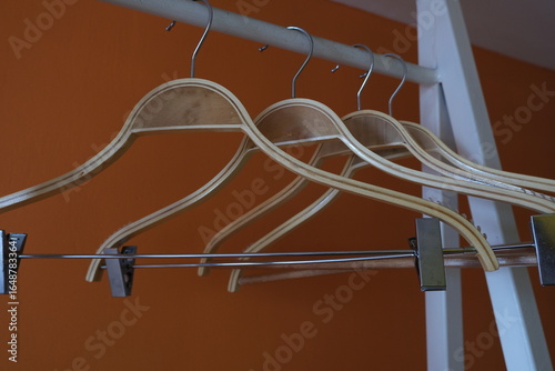 Tableau sur toile Several wooden hangers neatly arranged on a metal clothing rack against an orange wall, symbolizing minimalism or wardrobe organization