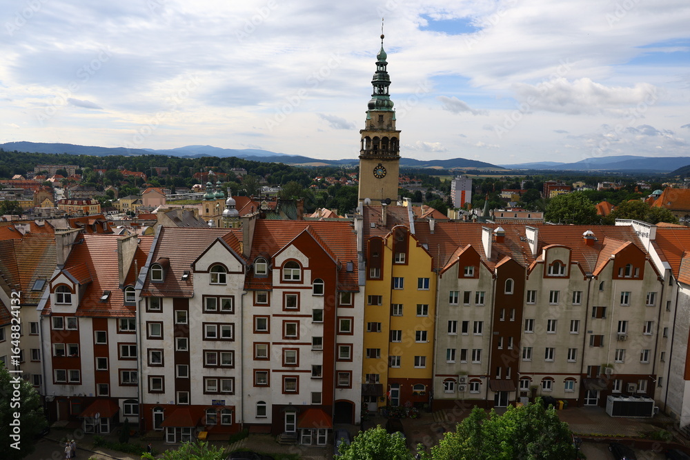 Obraz premium Colorful residential buildings and historic town hall tower in Kłodzko, Poland, with mountain landscape in the background