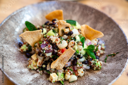 Bunter Quinoa-Salat mit schwarzen Bohnen, Mais, Tomaten, Kräutern und knusprigen Tortilla-Chips auf einem rustikalen Keramikteller
