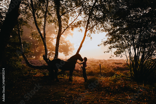 A girl with her horse in the woods during sunrise