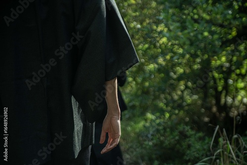 A samurai in black kimono is walking through forest.