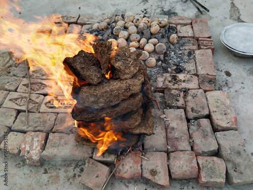 Round wheat flour balls being roasted on residual ashes of burnt cow dung cakes in traditional Indian village method, showing post-fire slow cooking technique used for preparing litti