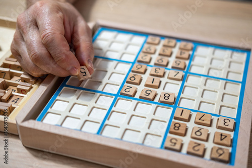 closeup hands carefully placing number into Sudoku puzzle, senior man focused on solving puzzle on wooden board, Brain exercise, cognitive health, and mental agility in mature age, brain health