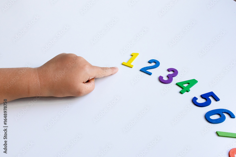 Fototapeta premium Child learning numbers with colorful foam digits on white background