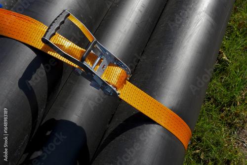 Valokuva Close-up of black plastic pipes secured with an orange ratchet strap for transportation or storage
