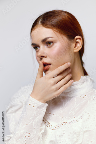 Young woman in a white lace blouse contemplating emotions with a soft expression on a neutral background, ideal for fashion or beauty concepts