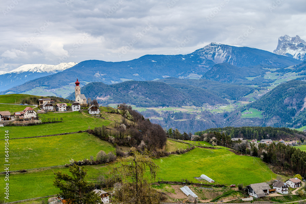 Obraz premium Alpine spring view with a distant church seen from near Klobenstein, Ritten, Eisacktal valley, South Tyrol, Italy