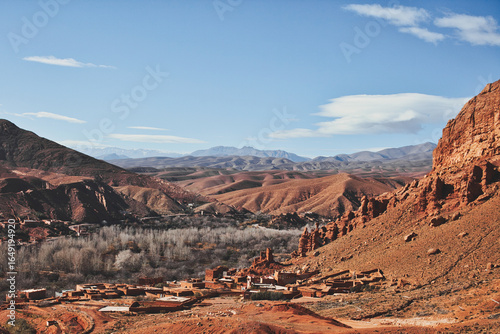 Traditional mud-brick town in Morocco nestled among barren rocks with a lush green oasis in the valley, scenic desert landscape and cultural travel destination