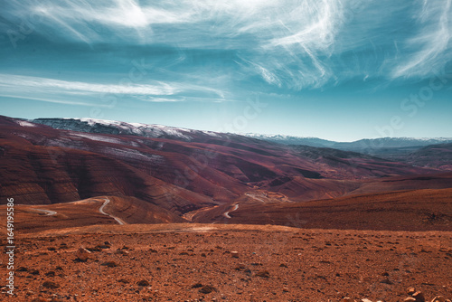 Scenic winding road through arid desert valley in Tagherghist, Morocco, under a turquoise sky with scattered clouds