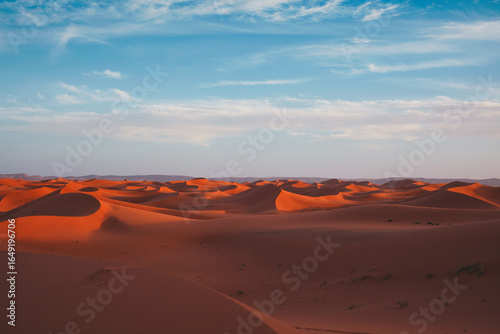 Endless sand dunes of the Lion Dune, Morocco – vast desert landscape at red sunset, dramatic sky over rolling dunes, serene and majestic Sahara desert scenery
