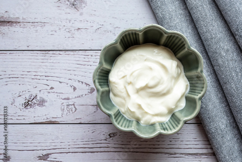 Green bowl with natural yogurt on the white wood table with napkin.