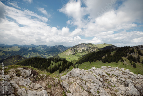 Mountain Panorama with Rocky Foreground and Rolling Green Hills under Cloudy Sky