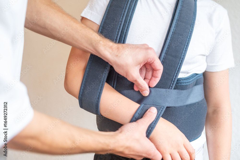 Obraz premium Teen boy in an orthopedic sling, Medical professional fitting therapeutic support belt on patient during rehabilitation session, showcasing personalized healthcare approach