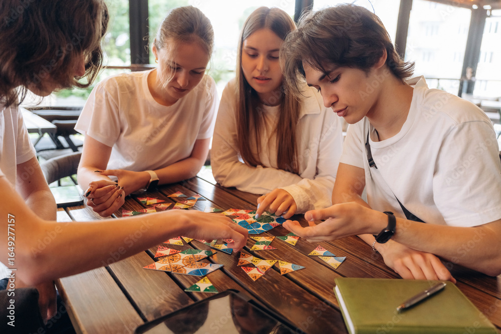 Fototapeta premium Playing the game at the table. Group of young friends are in the cafe restaurant