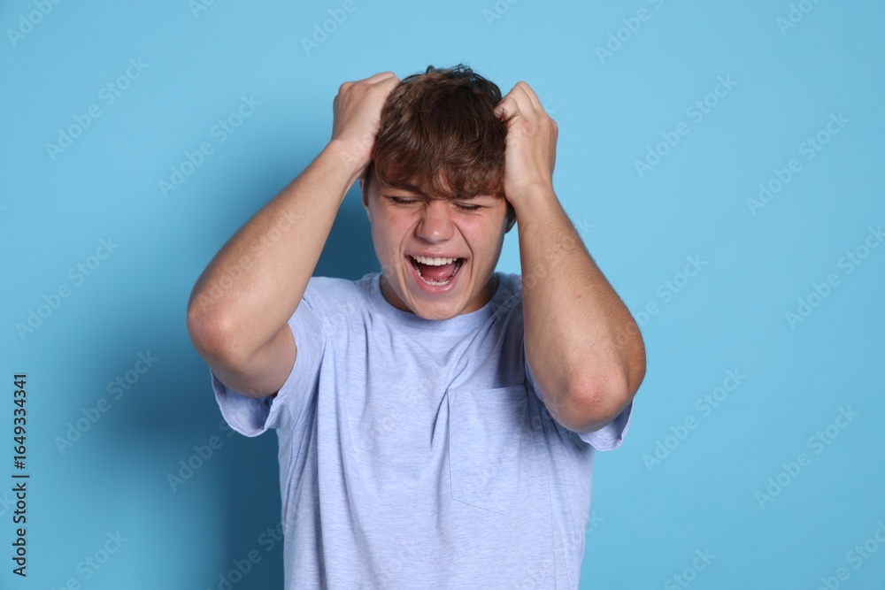Fototapeta premium Teenage boy suffering from panic attack on light blue background
