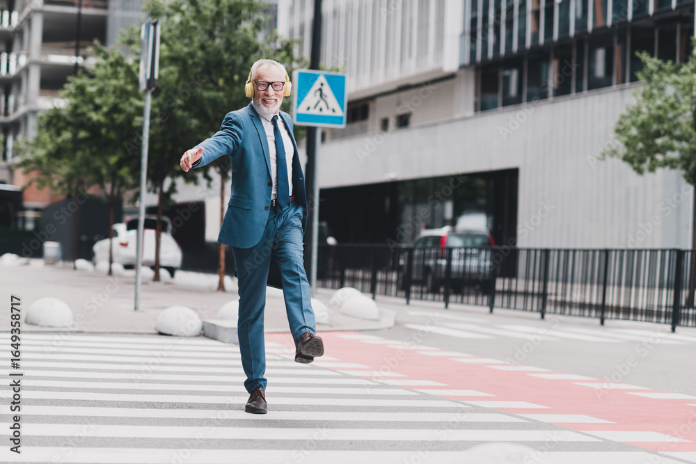 Obraz premium Confident businessman walking outdoors in a city street, wearing formal suit and headphones while smiling and enjoying the day