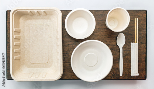 Eco friendly disposable tableware set includes tray, bowls, cup, spoon, and chopsticks on wooden surface, promoting sustainability