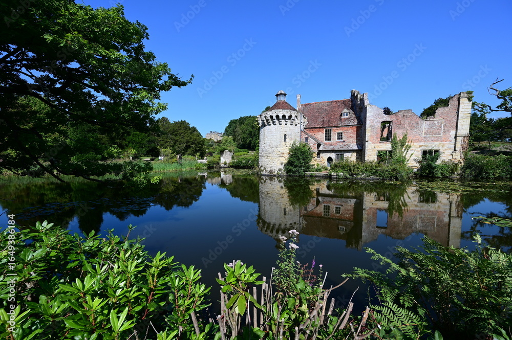 Obraz premium Ruins of a Medieval Moated Manor house by a lake in summertime.
