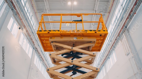 Yellow scissor lift platform extending in bright industrial building, high angle view