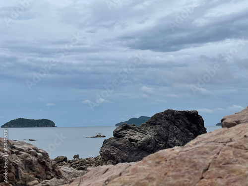 A serene coastal view featuring rocky foreground, calm waters, and distant islands under a cloudy sky.