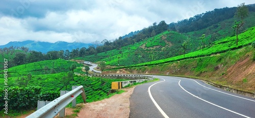 A passenger bus from distance navigates the winding curves of the scenic Gap Road of Munnar, kerala, india, surrounded by vibrant green tea plantations and mist-covered hills, offering a picturesque