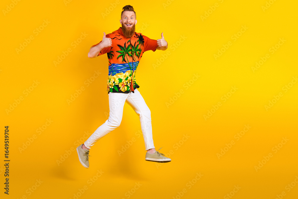 Fototapeta premium Energetic Young Man Wearing Tropical Shirt and White Pants Posing on Bright Yellow Background While Giving Thumbs Up
