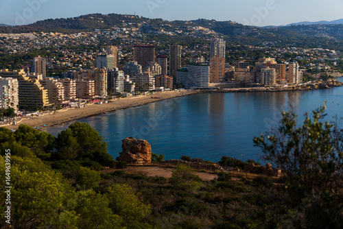City Meets Nature in Calpe, a panoramic morning view of Calpe City Bay, where a serene nature reserve and calm blue sea lead the eye to the city's buildings in the distance