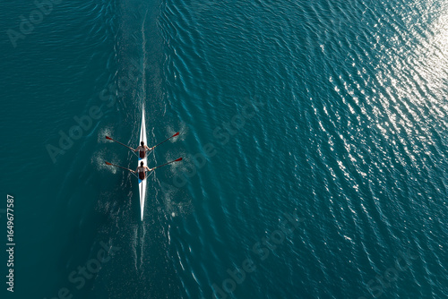 Two synchronized rowers glide across calm water in perfect aerial symmetry