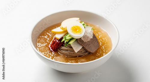 A bowl of traditional Korean cold noodles, Naengmyeon, with beef, egg, cucumber, and pear in a chilled, icy broth.