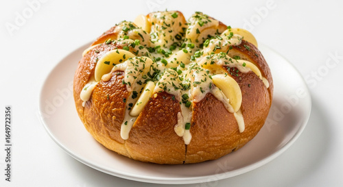 A freshly baked Korean cream cheese garlic bread loaf, filled with creamy sauce and topped with garlic slices and chopped herbs, on a white plate.