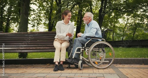 Woman and elderly man sit on park bench looking at smartphone