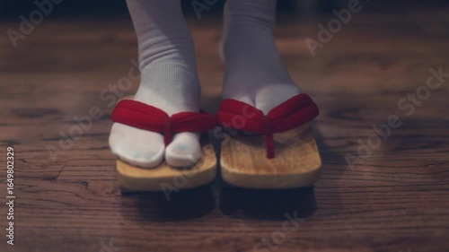 A woman putting on traditional Japanese shoes, such as geta or zori, captured in a close-up moment. The image highlights cultural detail and graceful movement, with attention to traditional attire and