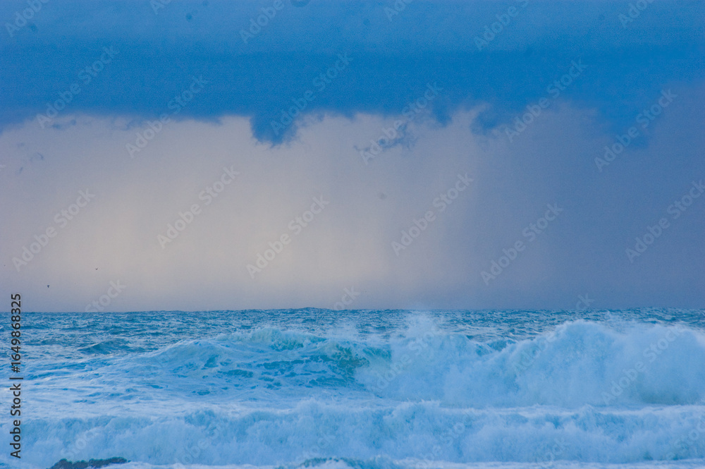 Obraz premium Waves crashing in the ocean under a cloudy sky.
