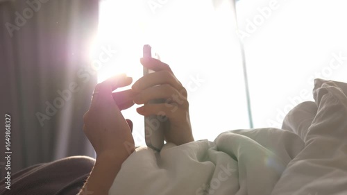 Close-up of a man's hands lying in bed and checking chats on his smartphone, browsing through mail and reading the news. Smartphone addiction