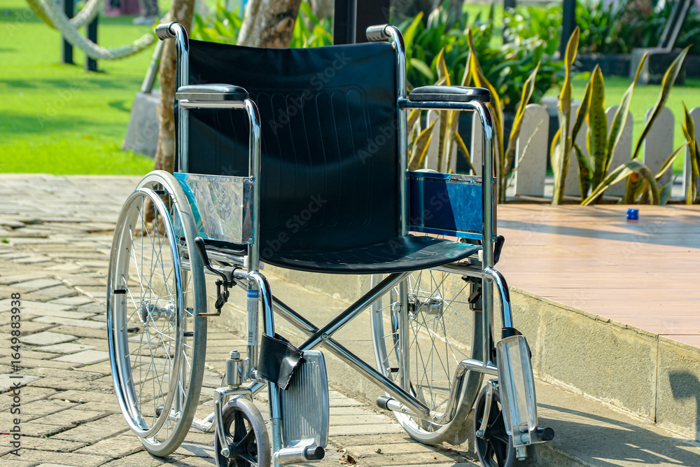 Fototapeta premium Empty Silver Wheelchair on Stone Path in Green Park