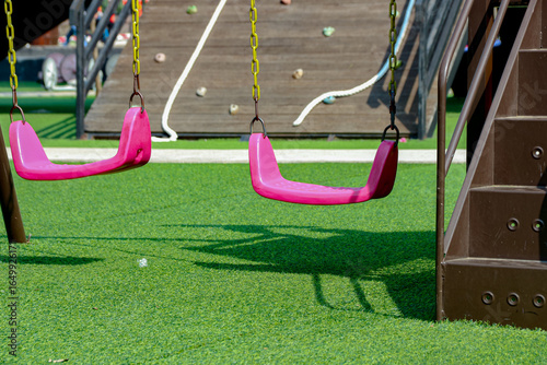 Empty Pink Swings Hanging on Outdoor Playground with Green Turf