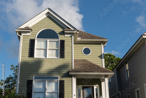 Isle of Palms, South Carolina, USA - June 30, 2025: A light green two-story coastal home with black shutters and distinctive arched and circular windows, under clear summer skies at Wild Dunes Resort