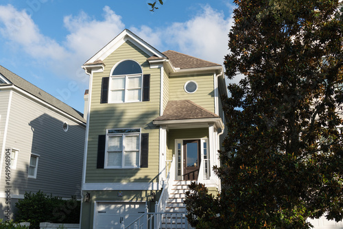 Isle of Palms, South Carolina, USA - June 30, 2025: A light green two-story coastal home with black shutters and distinctive arched and circular windows, under clear summer skies at Wild Dunes Resort