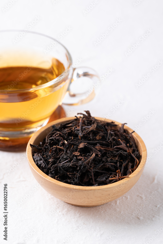Dried black tea leaves in wooden bowl and hot tea in cup glass on white background, Healthy herbal drink Dried black tea leaves in wooden bowl and hot tea in cup glass on white background, Healthy herbal drink