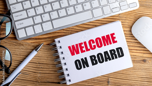 Welcome on board text on spiral notebook with pen, keyboard and mouse on wooden desk